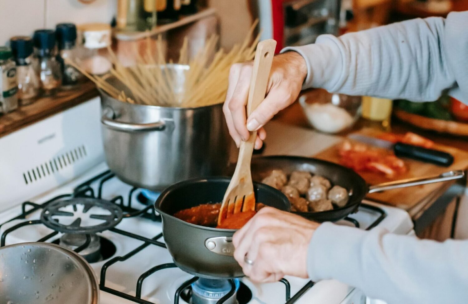 Person stirring homemade creamy pasta sauce in a saucepan on a busy kitchen stove.