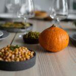 High angle of wooden table served with delicious chickpeas and fresh ripe pumpkin near empty plates and glasses for guests