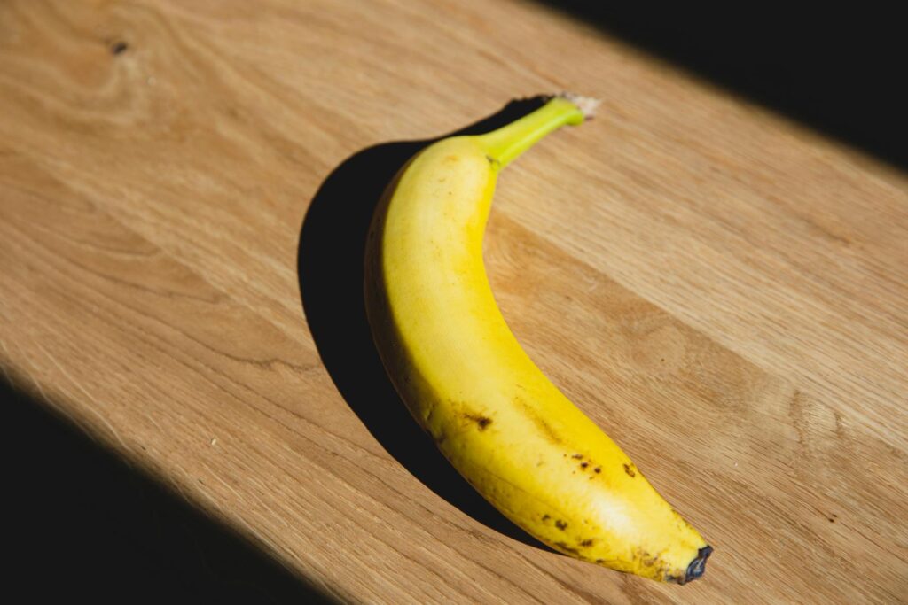 From above of ripe banana casting shadow placed on wooden board lightened by sunlight