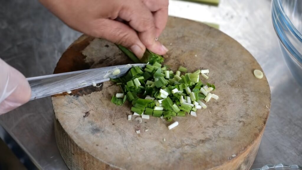 a person cutting up green onions on top of a wooden cutting board