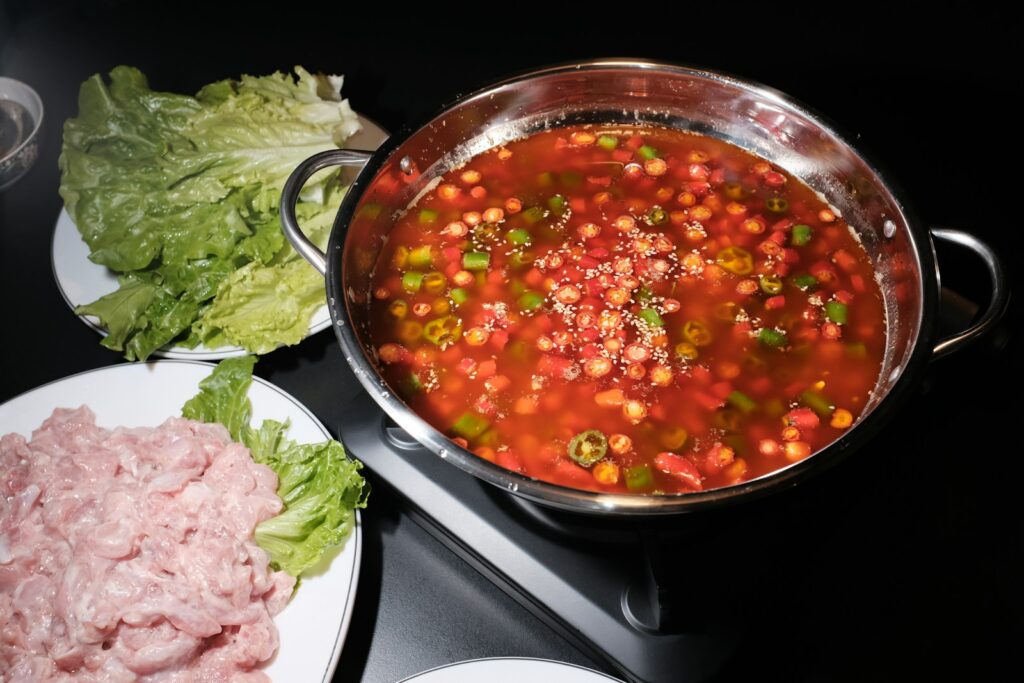a pot of soup next to a plate of meat and lettuce