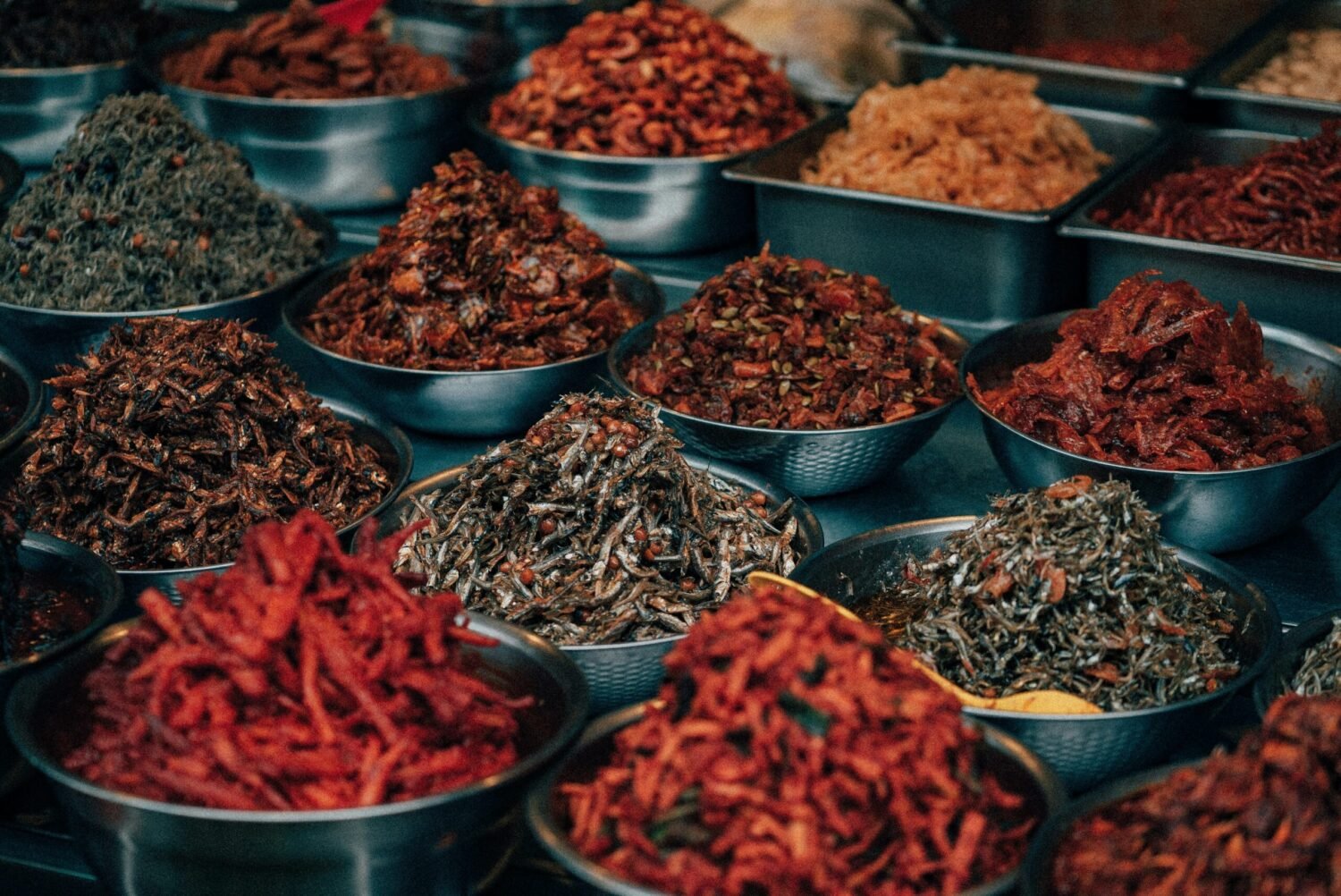 Metal bowls filled with a variety of preserved and seasoned dried ingredients, commonly used in Hawaiian crack seed snacks.