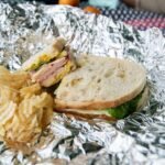 Stacked deli-style sandwich with tri-tip leftovers, lettuce, mustard, and chips on foil.