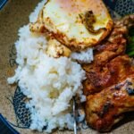 Hearty bowl of white rice topped with fried egg, seasoned chicken, and green garnish, perfect for a cozy Southern chicken and rice dinner.