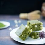 Close-up of matcha brownies with white chocolate chunks, served on a white plate with a decorative flower—an elegant dessert for matcha lovers.