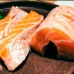Fresh salmon sashimi arranged on a plate with shredded daikon and green garnish, showcasing vibrant orange cuts.