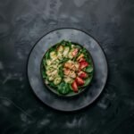 Colorful plate of grilled chicken salad with avocado, cherry tomatoes, cucumber, and spinach.