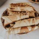A woven basket filled with traditionally wrapped Filipino tupig, made from glutinous rice and coconut, encased in banana leaves and tied with string—ready for grilling or steaming.