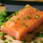 A fresh cut of raw salmon belly topped with chopped chives and herbs, ready to be transformed into a rich and buttery dish.