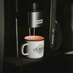 White ceramic mug filling with coffee under a black and silver single-serve coffee machine