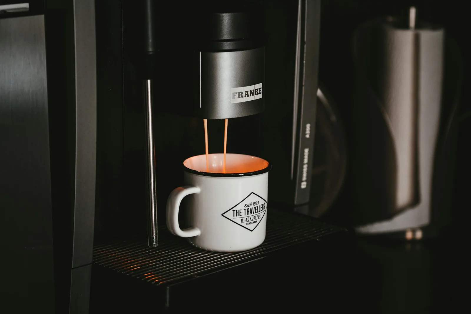 White ceramic mug filling with coffee under a black and silver single-serve coffee machine