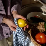 Hands wiping a lemon with a striped cotton kitchen towel, a reusable alternative to paper towels