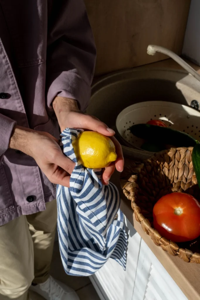 Hands wiping a lemon with a striped cotton kitchen towel, a reusable alternative to paper towels